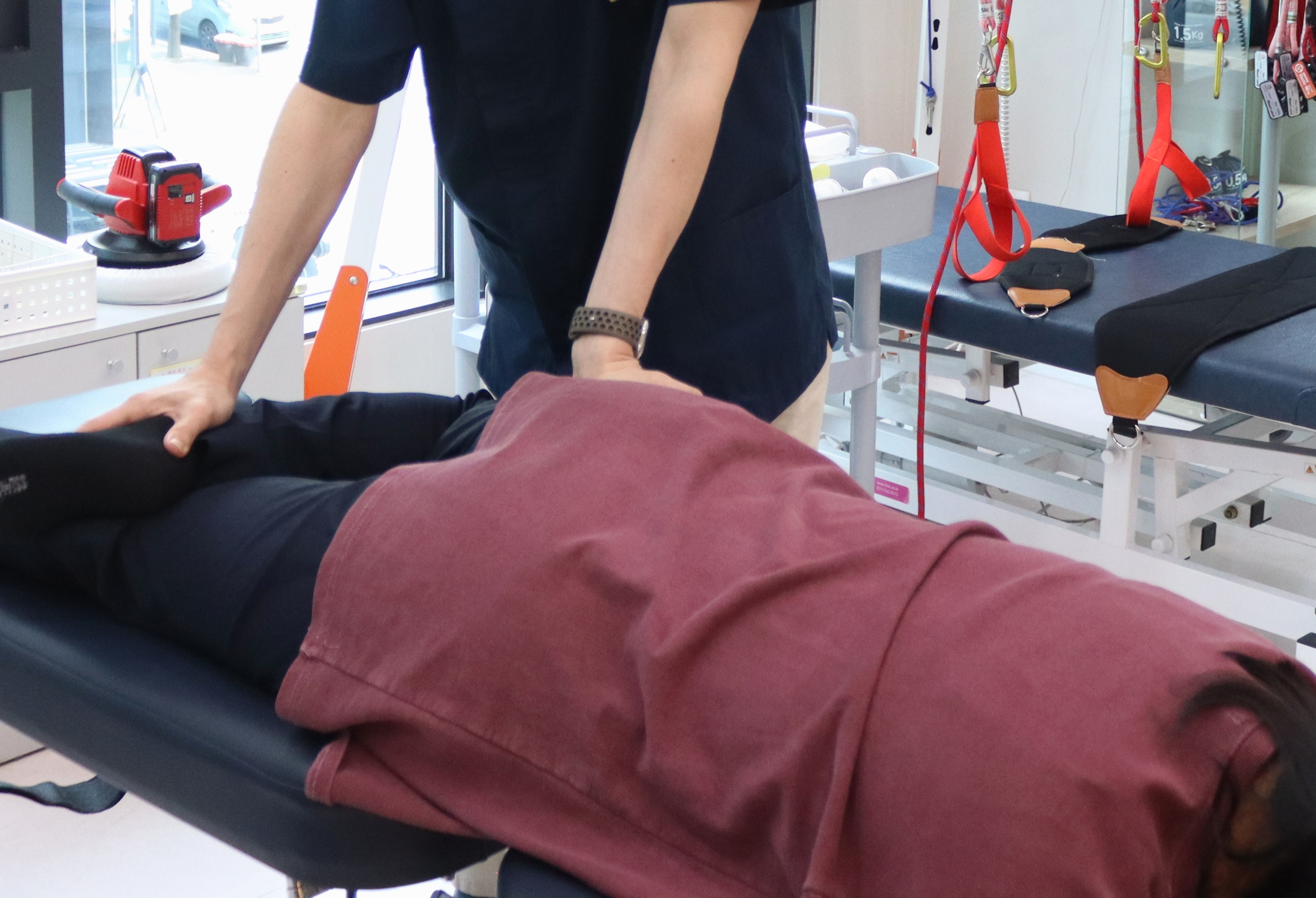 치료대에 옆으로 누운 환자의 골반과 허벅지를 원장이 손으로 잡아 교정하는 추나 치료 장면